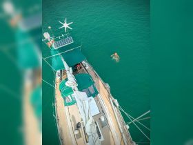 An aerial view of a person swimming in clear turquoise waters beside a sailboat, showcasing the perfect blend of adventure and relaxation on the water.