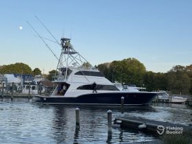 A stunning fishing yacht named 'Barbaric' is docked, showcasing its impressive structure against a serene backdrop of trees and a clear sky.