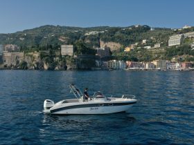 A sleek speedboat navigates the serene waters with a picturesque coastal backdrop, showcasing the beauty of the landscape and the vessel's design.