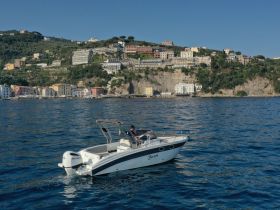 A sleek speedboat navigates the clear waters, showcasing stunning coastal views of colorful buildings and lush hillsides in the background.