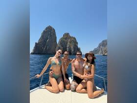 A cheerful group of friends enjoys a sunny day on a boat, surrounded by stunning rock formations — perfect for a memorable beach outing.