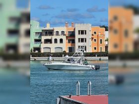 A fishing boat navigates through a scenic waterway, with colorful buildings in the background, showcasing a vibrant coastal atmosphere.