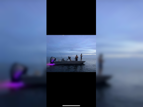 A group of friends enjoys an evening fishing trip on a boat, casting lines into the calm ocean waters under a twilight sky.
