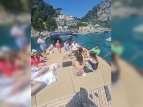 A lively group enjoys a sunny day on a yacht, sharing cocktails and snacks while soaking up the beautiful coastal views.