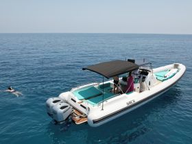 A swimmer enjoys the clear blue waters next to a sleek boat, while another person is at the helm, showcasing a perfect day on the water.