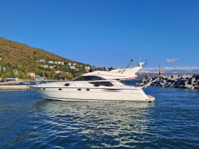 A sleek yacht docked in a picturesque harbor, surrounded by lush hills and clear blue skies, perfect for luxury boating experiences.