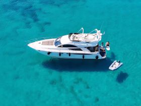 An aerial view of a luxurious yacht anchored in stunning turquoise waters, with guests paddleboarding nearby — a perfect scene for water activities and relaxation.