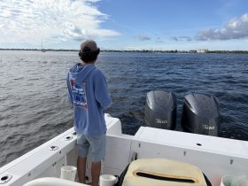 A young man stands on the deck of a boat, casting a line into the water, enjoying a day of fishing on the open sea.