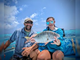 A joyful moment captured as a young girl and an adult proudly display their catch while fishing in the ocean — a perfect highlight of a fun day on the water.