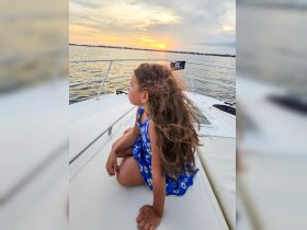 A young girl enjoys a serene sunset view from the deck of a boat, capturing the essence of family adventures on the water.