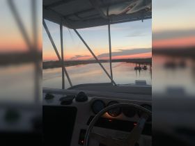 A serene view from the helm of a boat, showcasing the tranquil waters and a colorful sunset — perfect for evening cruises.