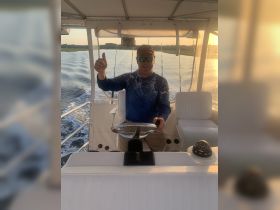 A smiling captain gives a thumbs up while at the helm of a boat, showcasing the interior console and seating area — perfect for a day on the water.