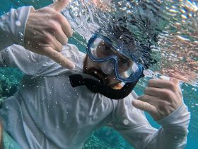 A snorkeler gives a shaka sign while exploring vibrant underwater scenery, capturing the excitement of marine adventures.