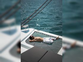 A man relaxes on the netting of a catamaran, enjoying the sun and sea — a perfect moment for leisure on the water.
