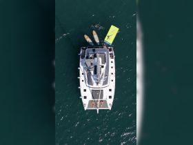 Aerial view of a lively group enjoying paddleboarding and swimming around a catamaran, showcasing the perfect day on the water.