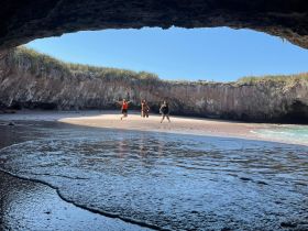 A group of friends joyfully jumps on the sandy beach inside a stunning cave, capturing the essence of adventure and fun in a picturesque setting.