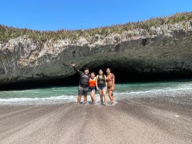A joyful group of friends poses at the beach, enjoying the sun and surf near a stunning rock formation — perfect for memorable beach outings and adventures.
