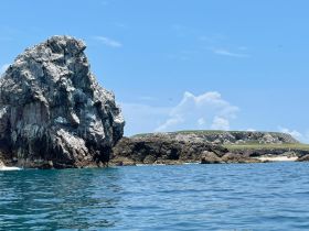 A stunning view of a prominent rock formation against a clear blue sky, showcasing the natural beauty of the coastline — perfect for scenic boat tours.