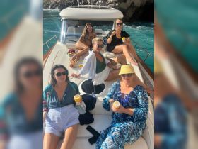 A lively group of friends enjoys a sunny day on a yacht, indulging in snacks and cocktails while soaking up the beautiful surroundings — perfect for a fun getaway.