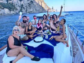 A joyful group celebrates aboard a yacht, enjoying food and drinks while surrounded by stunning coastal views — perfect for family gatherings or special occasions on the water.