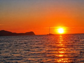 A serene sunset view featuring a sailboat silhouetted against the vibrant orange sky, perfect for capturing the beauty of evening cruises.