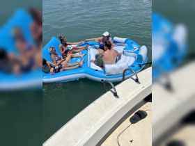 A lively group enjoys a sunny day on a floating mat, engaging in fun activities in the water — perfect for summer outings and relaxation.