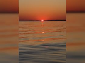 A stunning sunset reflects on the calm waters, creating a picturesque scene perfect for romantic evenings or peaceful boat rides.