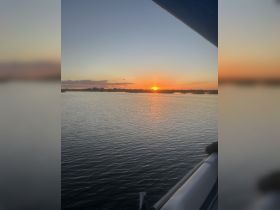 A serene sunset view over calm waters, framed by the edge of a boat, creating a picturesque scene perfect for evening cruises.