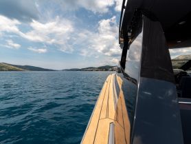 A stunning side view of a sleek yacht gliding through calm waters, showcasing the beautiful coastline and clear blue skies — perfect for luxury boating experiences.