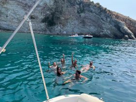 A lively group enjoys a refreshing swim in crystal-clear waters, surrounded by stunning cliffs — perfect for summer adventures and beach outings.