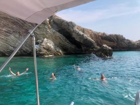 A group of friends enjoys a refreshing swim in crystal-clear waters near a rocky coastline, capturing the essence of summer adventures on the water.