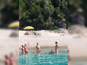 A lively group of friends enjoys a sunny day swimming in crystal-clear waters, capturing the essence of summer fun at the beach.