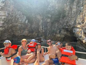 A cheerful family enjoys a boat trip, wearing life jackets and posing for a photo against a stunning rocky backdrop — perfect for adventurous outings and family bonding on the water.