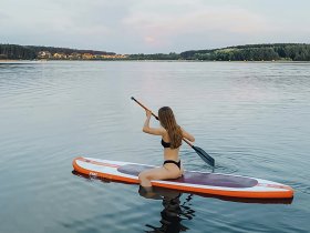 A woman paddleboards on calm waters, enjoying a serene outdoor experience surrounded by nature — perfect for adventure seekers and water sports enthusiasts.