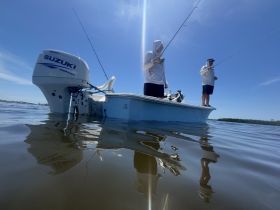 Two anglers stand on a fishing boat, casting their lines into the calm waters, showcasing a perfect day for fishing adventures.