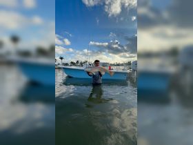 A fisherman proudly displays his catch, a large redfish, while standing in the water next to his boat — a perfect moment for fishing enthusiasts.