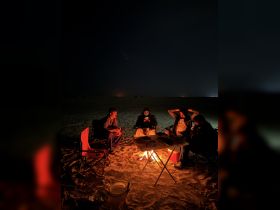 A group of friends gathers around a campfire at night, enjoying each other's company under the stars — perfect for outdoor adventures and bonding experiences.