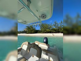 A scenic view from a boat with clear turquoise waters and a sandy beach in the background, featuring a person walking along the shore — perfect for showcasing a relaxing day on the water.