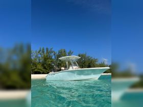 A stunning Key West center console boat glides through crystal-clear waters, showcasing its sleek design against a backdrop of lush greenery and a sandy beach.