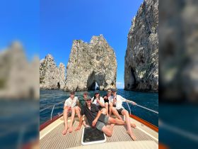 A lively group enjoys drinks aboard a boat near the iconic rock formations of Cabo San Lucas, capturing the essence of a fun day on the water.