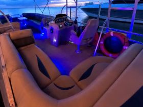 Interior view of a stylish boat cabin featuring comfortable seating and a helm, illuminated by ambient blue lighting, perfect for evening cruises.
