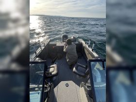 A person is seated at the helm of a fishing boat, preparing for a day on the water. The interior showcases comfortable seating and a well-equipped console, ideal for fishing adventures.