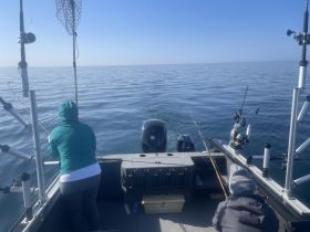 Two individuals enjoy a fishing trip on a boat, casting their lines into the calm waters — a perfect day for angling enthusiasts.