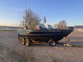 A side view of a Lund 1875 Fisherman boat on its trailer, showcasing its sleek design and fishing gear, perfect for anglers looking to hit the water.