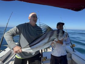 Two anglers proudly display their impressive catch while fishing on a boat, showcasing the thrill of deep-sea fishing adventures.