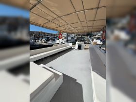 Interior view of a spacious lounge area on a boat, featuring comfortable seating and a shaded canopy, perfect for relaxing while docked.