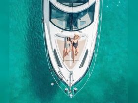 Two friends relax and sunbathe on the deck of a luxurious yacht, surrounded by stunning turquoise waters — a perfect scene for summer getaways and relaxation on the water.
