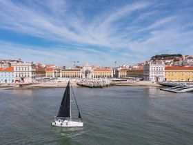 A picturesque view of a sailboat navigating the waters of Lisbon, with stunning historical architecture in the background — a perfect representation of urban sailing adventures.