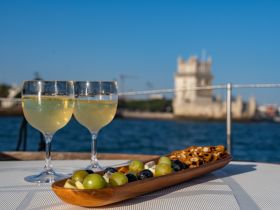 A refreshing setup featuring cocktails and a platter of snacks on a boat, with a scenic backdrop of a historic tower — perfect for enjoying leisurely moments on the water.