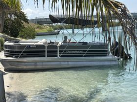A sleek Berkshire pontoon boat docked in clear waters, surrounded by lush greenery — perfect for leisurely outings and family fun on the water.